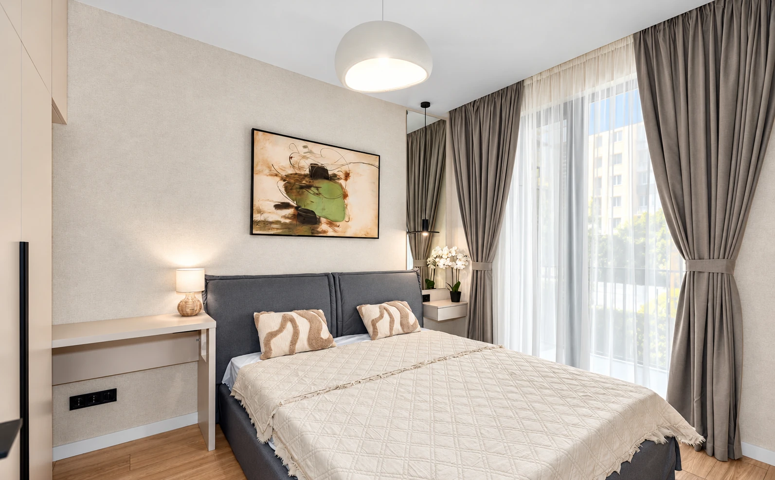 საძინებელი ნაცრისფერი საწოლის თავით, რბილი ქსოვილებითა და დიდი ფანჯრით